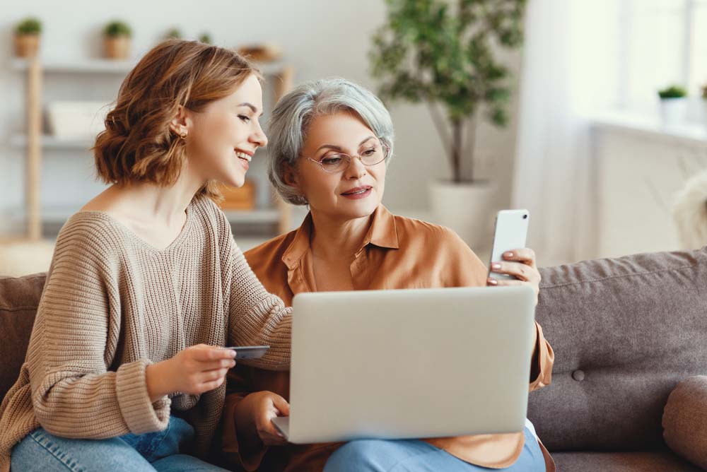 Protect your computer. Two women using a laptop and mobile phone with a debit card in the hand of the woman on the left.