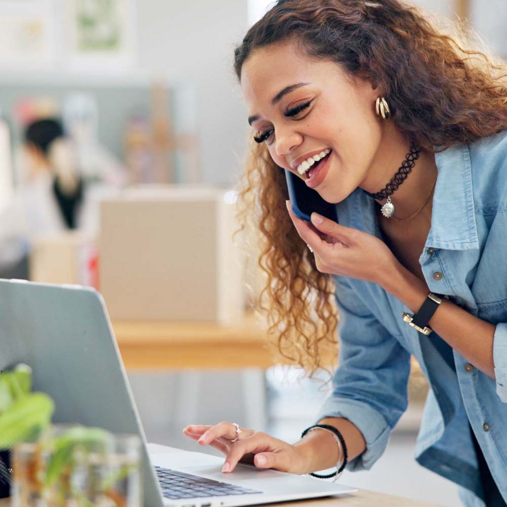 Remote computer repairs. Photo is of a smiling woman using the phone in front of her laptop.